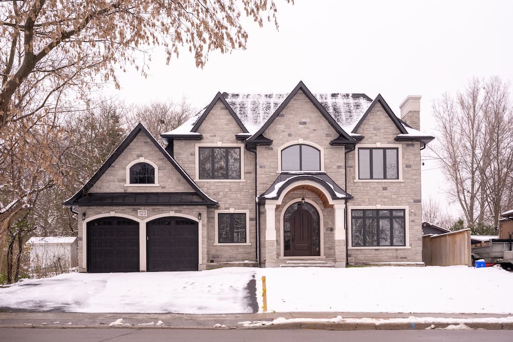 A large newly-built stone-and-brick two-storey family home with a double garage on a snowy winter day in Brooklin