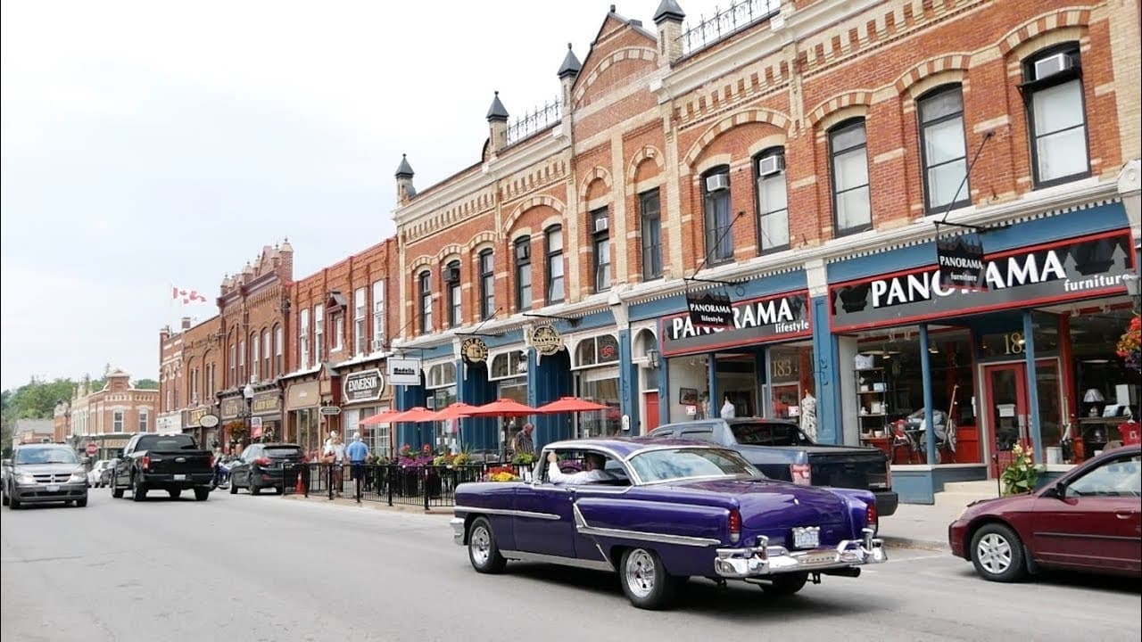 Heritage brick storefronts and patios along historic Queen Street in downtown Port Perry, with a classic car passing by