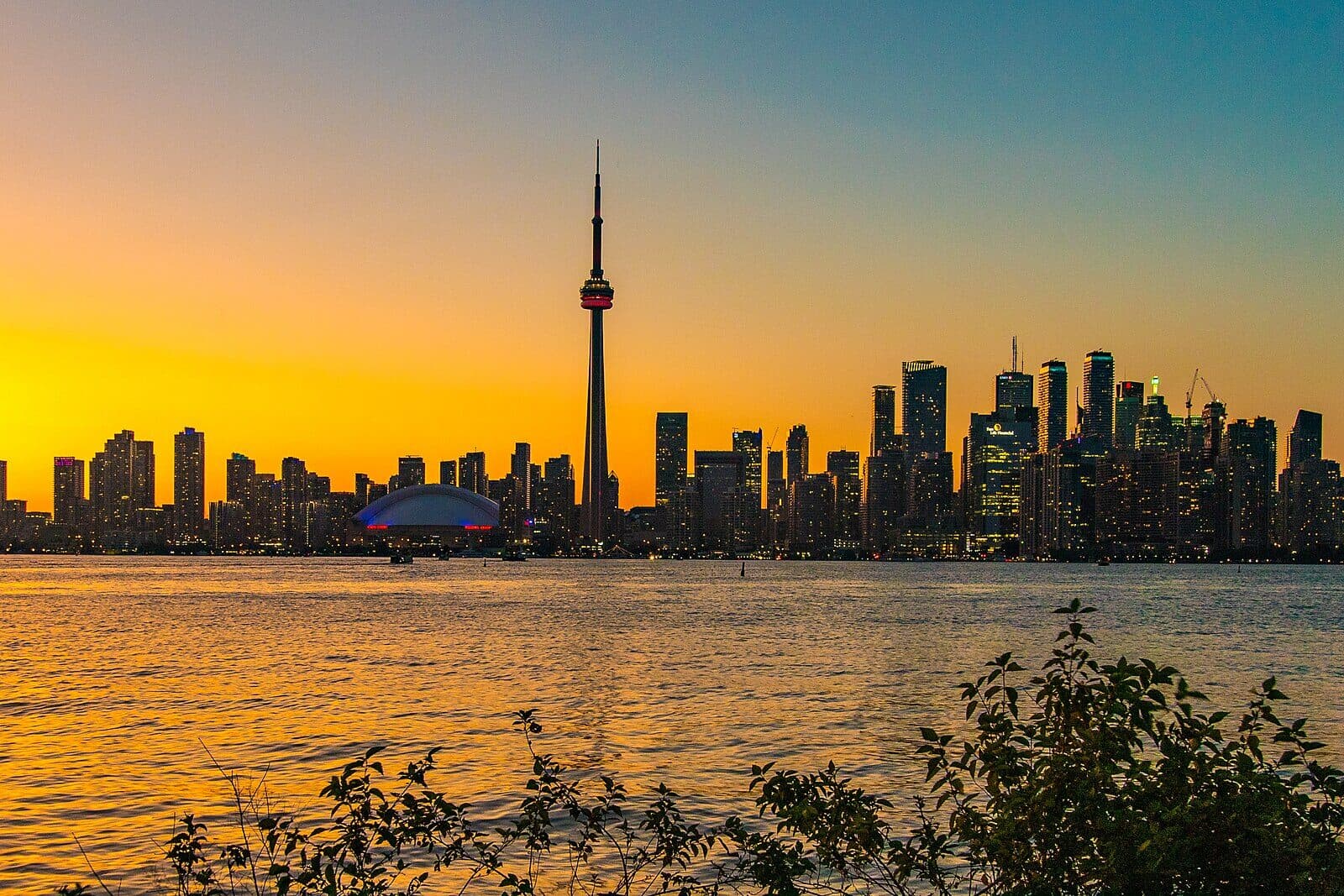 Toronto's downtown skyline and CN Tower silhouetted against a vivid orange sunset over Lake Ontario