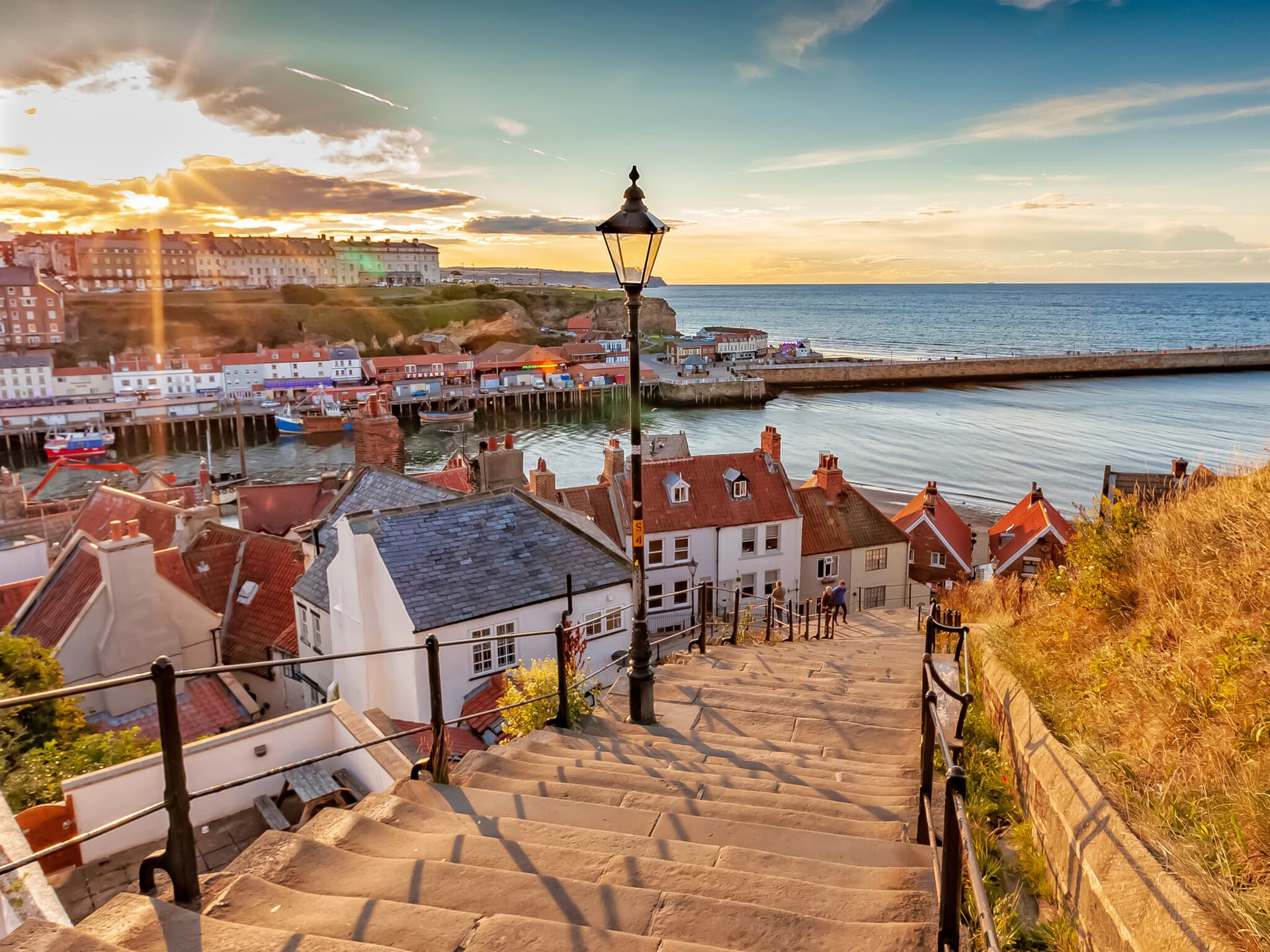 Stone steps descending to the harbour at golden hour in Whitby, lined with historic waterfront homes and fishing boats